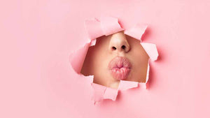 Persoon blaast een kus door roze gescheurd papier een visual voor Luxury Lashes blog Alles over wimperextensions de basis.