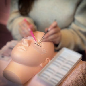 Een oefenhoofd op een tafel, terwijl iemand wimpers aanbrengt op het model met luxury lashes tweezers