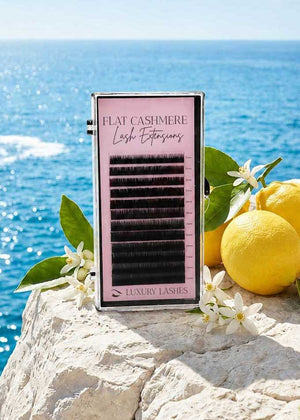Luxury Lashes Flat Cashmere wimperextensions op witte rotsen met citroenen, bloemen en zeezicht in luxe Mediterranean summer setting.