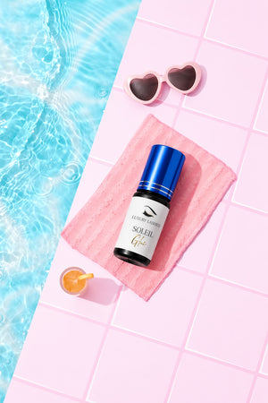 Soleil Glue eyelash extension adhesive with blue cap in mini pool studio setting with cocktail, towel and heart sunglasses